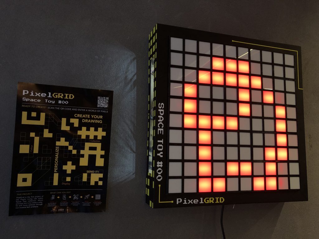 Interactive pixel-art LED display glowing in a plaza at night with people interacting